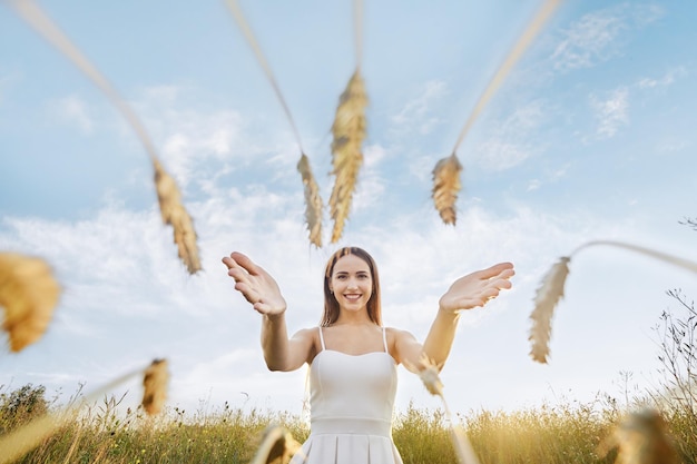 Happy woman stretches her hands to the ears of wheat