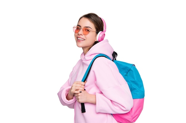 Happy woman student in pink hoodie listening to audio course in headphones carrying school bag