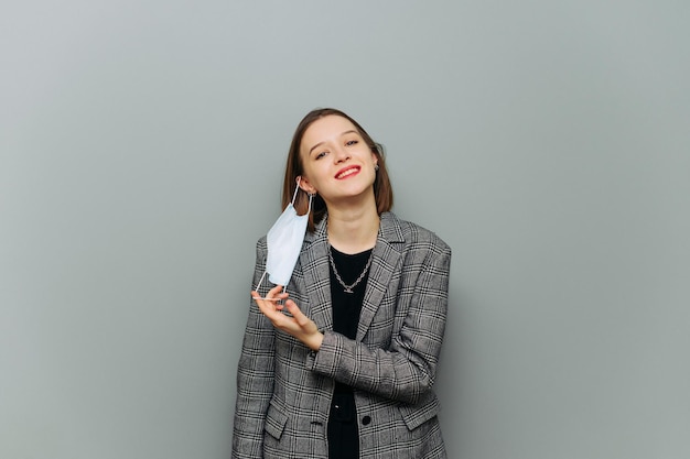 Happy woman in stylish formal clothes removes protective\
medical mask from face