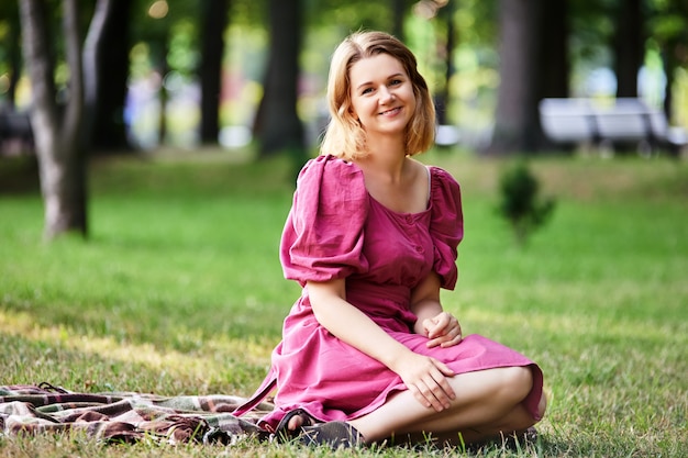 夏のドレスの幸せな女性は公園の芝生の上に座っています