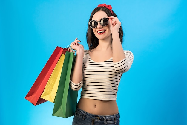 The happy woman in sunglasses holding color bags on the blue background