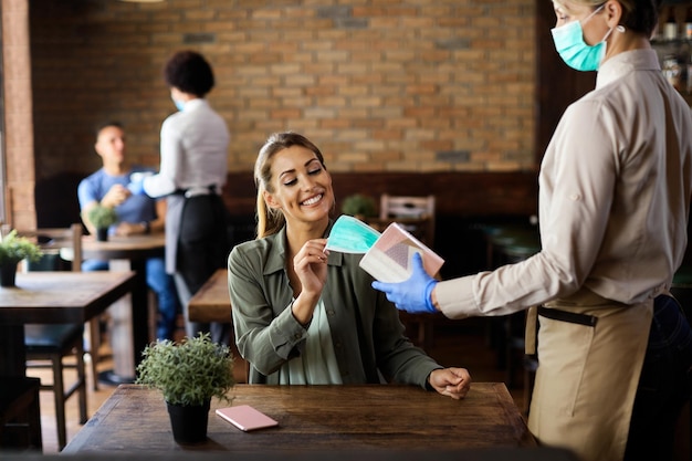 Happy woman taking protective face mask from waitress in a cafe