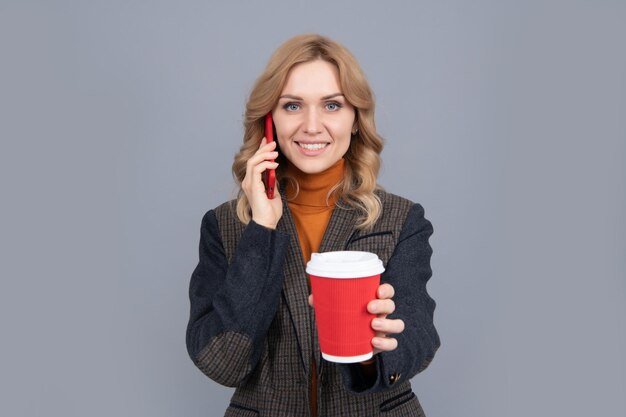 Happy woman talk on mobile phone giving hot cup grey background, tea.