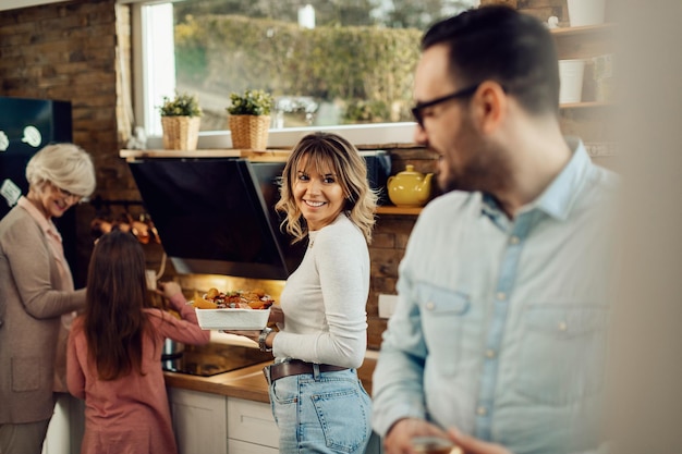 Happy woman talking to her husband while preparing food with her daughter and senior mother in the kitchen