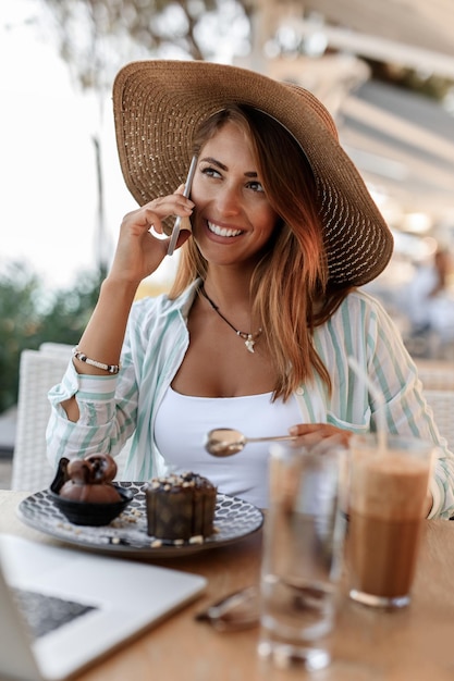 カフェでデザートを食べながら携帯電話で話している幸せな女性