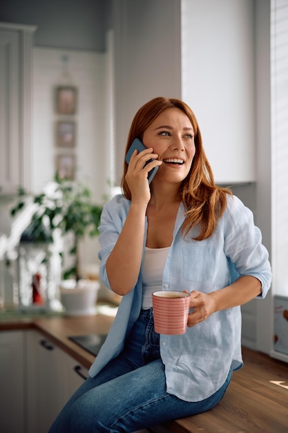 家でコーヒーを飲みながら電話で話す幸せな女性