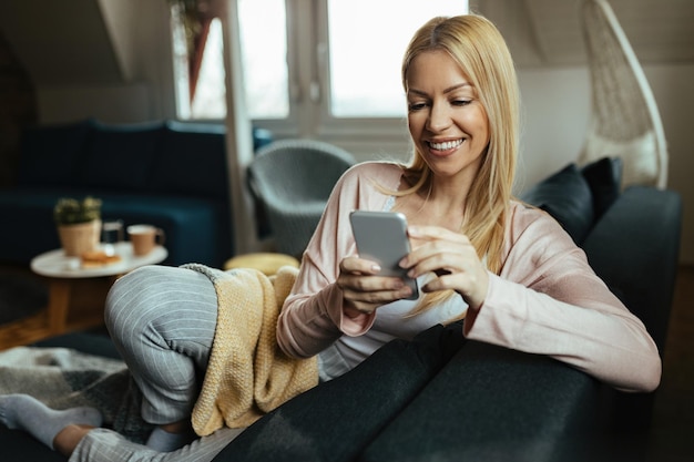 Messaggi di testo donna felice sul telefono cellulare mentre ci si rilassa nel soggiorno