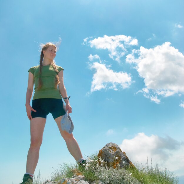 Donna felice sulla cima di una montagna con cielo azzurro e nuvole