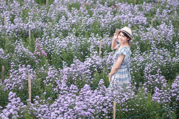 파란 드레스를 입은 행복한 여성 관광객은 보라색 마가렛 꽃 정원 여행 자연 휴가 및 휴가 개념에서 즐깁니다.