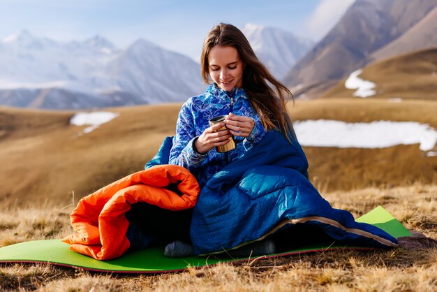 Happy woman tourist drinks tea on a background of beautiful mountains