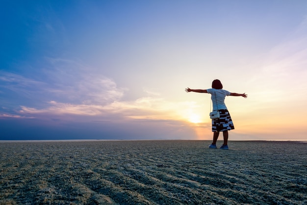 Happy woman tourist standing arms outstretched on the beach during sunset at Samui island