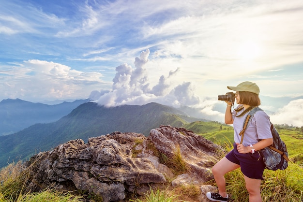 Счастливая женщина путешествует по Азии, держа камеру DSLR съемки фото красивый пейзаж природы на вершине горы на закате, путешественник путешественник азиатская девушка подростков, походы в лесной парк Пху Чи Фа, Чианграй, Таиланд