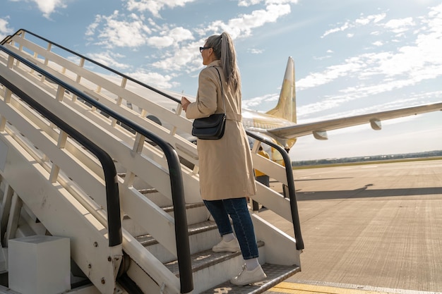 サングラスをかけた幸せな女性旅行者が空港で搭乗中に航空機の階段で立ち上がる