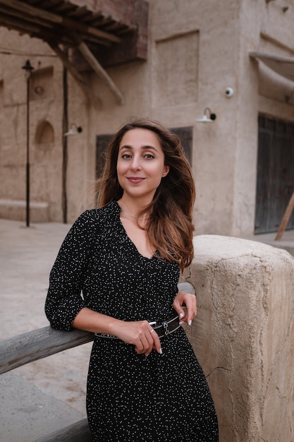 Happy woman traveler wearing black dress walking through the streets of an old Arab town or village in the middle of the desert. 