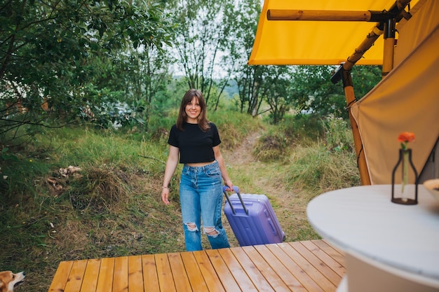 Happy woman traveler with luggage moving towards bedroom of cozy glamping house Luxury camping tent for outdoor summer holiday and vacation Lifestyle concept