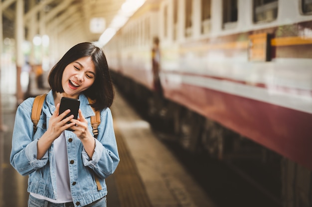 Happy woman traveler with smartphone at train station platform