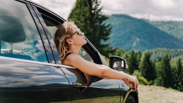 Happy woman travels by car in the mountains