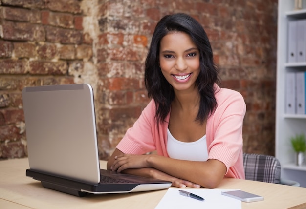 Happy woman using her laptop smiling at camera