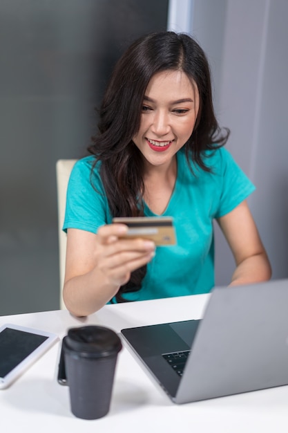신용 카드로 온라인 쇼핑을 위해 랩톱 컴퓨터를 사용하는 행복한 여자