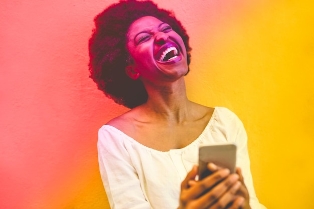 happy woman using mobile phone against wall