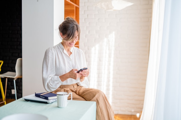 Happy woman using mobile phone while working at homeBeautiful lady browsing website on phone