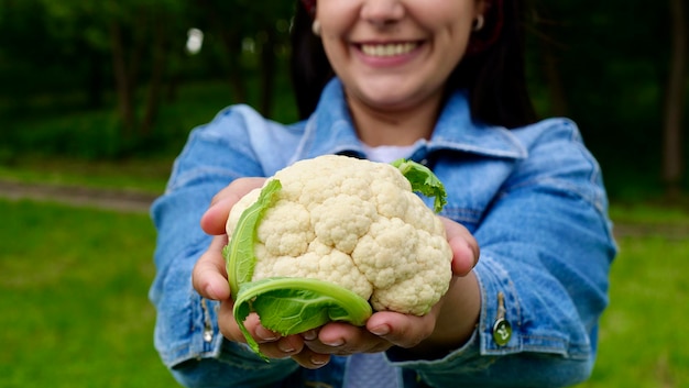 Happy woman vegetarian housewife keeps fresh cauliflower in her organic garden farmer with cauliflower during harvest Useful dietary vegetable close up