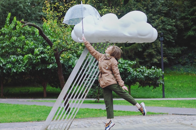 緑豊かな公園で傘を持って雨の中を歩く幸せな女性、微笑み、楽しい。ベンチに座る人