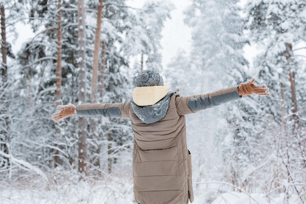 Happy woman walking in winter forest during heavy snowfall, watching falling snowflakes in park