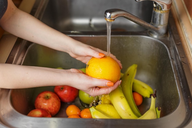 Happy woman washing fruit at kitchen bananas tangerines apples