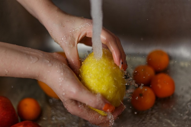 Happy woman washing fruit at kitchen bananas tangerines apples