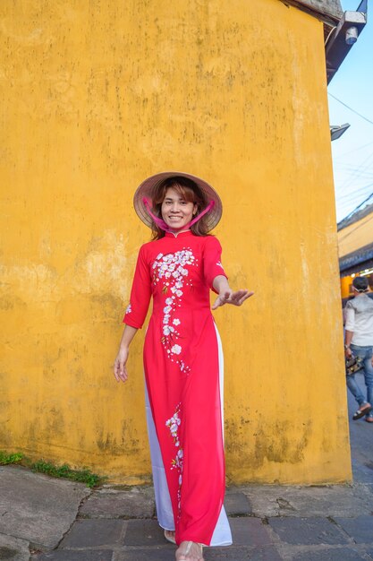 Happy woman wearing ao dai vietnamese dress and hat traveler sightseeing at hoi an ancient town in central vietnam landmark and popular for tourist attractions vietnam and southeast travel concept