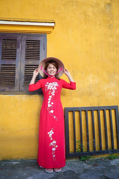 Happy woman wearing Ao Dai Vietnamese dress and hat traveler sightseeing at Hoi An ancient town in central Vietnam landmark and popular for tourist attractions Vietnam and Southeast travel concept