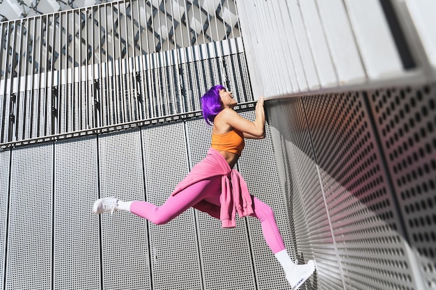 Happy woman wearing colorful sportswear climbing on the wall