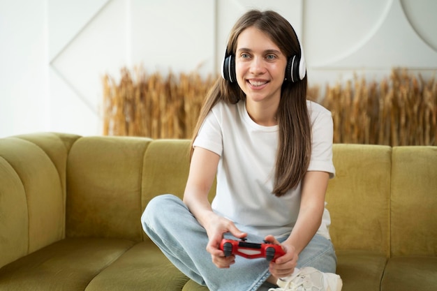 Photo happy woman wearing headphones uses a joystick to play a video game at home on the couch a joyful
