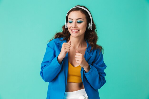 Happy woman wearing raincoat or jacket dancing while listening to music via wireless earphones