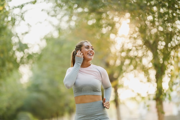 写真 スポーツウェアを着た幸せな女性が晴れた日に自然の中でジョギングをしています