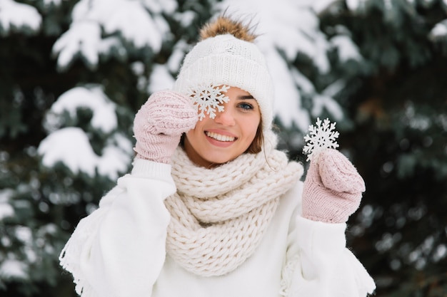 Happy woman in white winter clothes holding a beautiful snowflake in a park. 