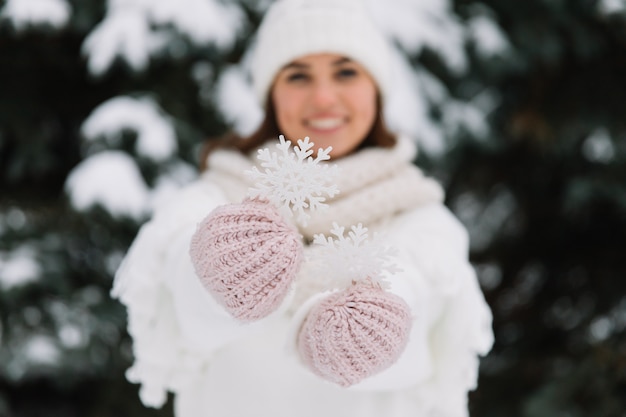 公園で美しい雪の結晶を保持している白い冬服で幸せな女は。