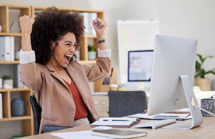 Photo happy woman winning on computer success bonus or celebration for news sales and business cheers in office wow yes and winner or biracial person celebrate fist pump and reading opportunity on pc