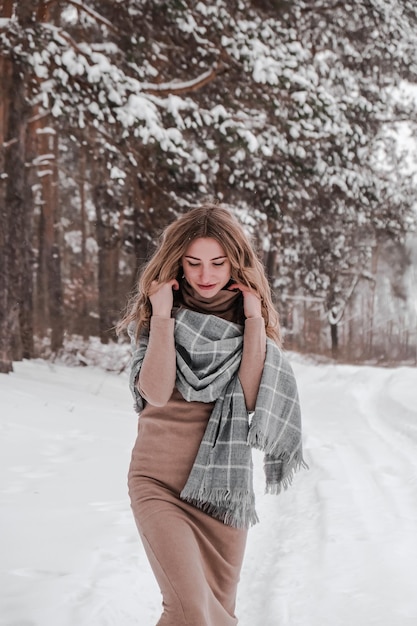 Счастливая женщина на фоне зимнего леса. Молодая красивая девушка в лесу на открытом воздухе. Портрет веселой красивой женщины. Зимняя мода. Платье с шарфом