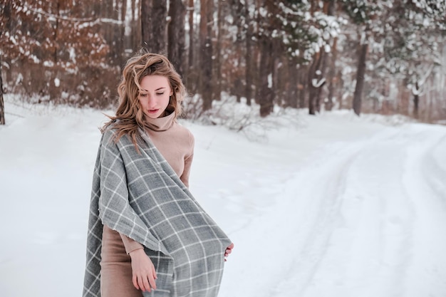 Happy woman on the winter forest background. Young pretty girl in the woods outdoors. Portrait of a cheerful beautiful woman. Winter fashion. Dress with scarf