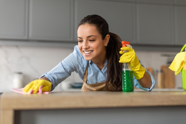 Foto donna felice che pulisce il bancone con spray e panno in cucina