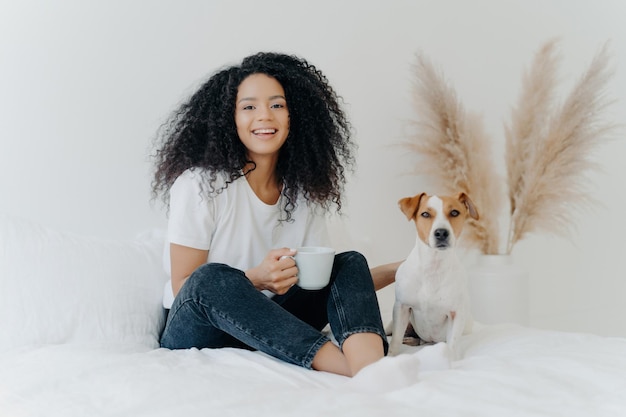 Happy woman with Afro hair tshirt jeans coffee mug genuine laughter Jack Russell terrier Cheerful teen with pet