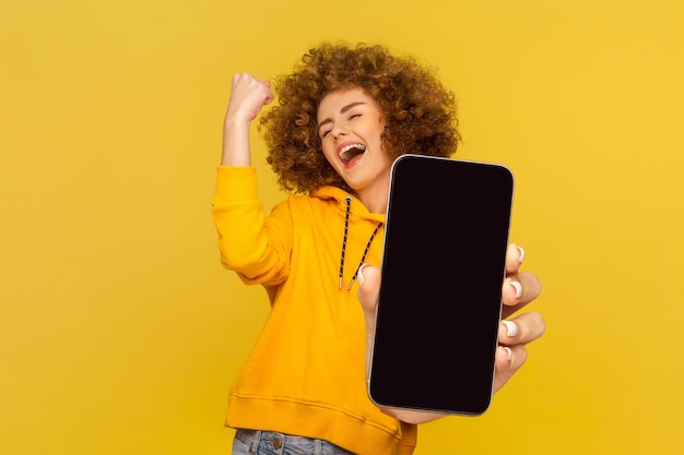 Happy woman with afro hairstyle showing big mobile display clenched fist celebrating victory