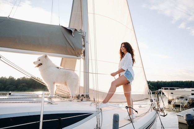 A happy woman with a big white dog on a white yacht in the sea.