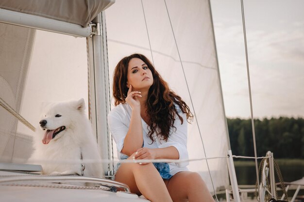 A happy woman with a big white dog on a white yacht in the sea.