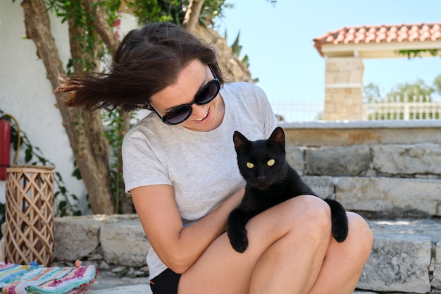 Happy woman with black cat, outdoor portrait of owner and pet.