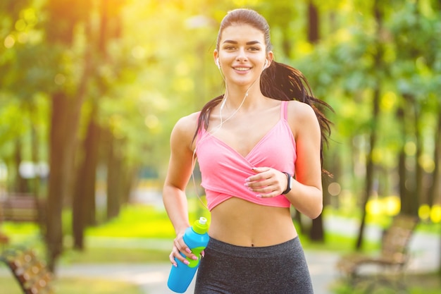 The happy woman with a bottle running in the park on the sunny background