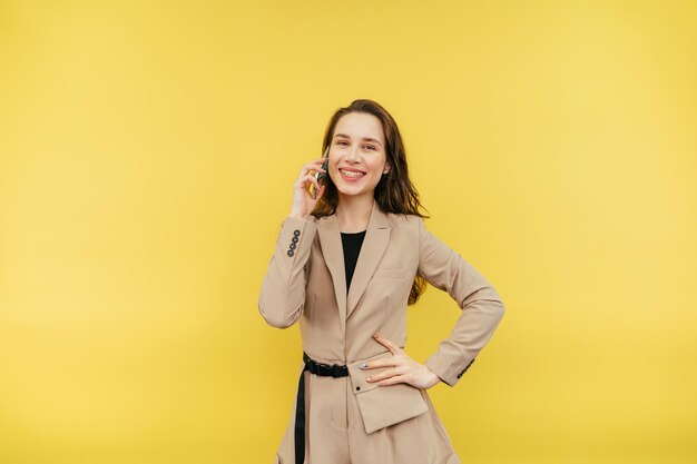 Happy woman with braces on her teeth and in a beige suit communicates on a smartphone with a smile