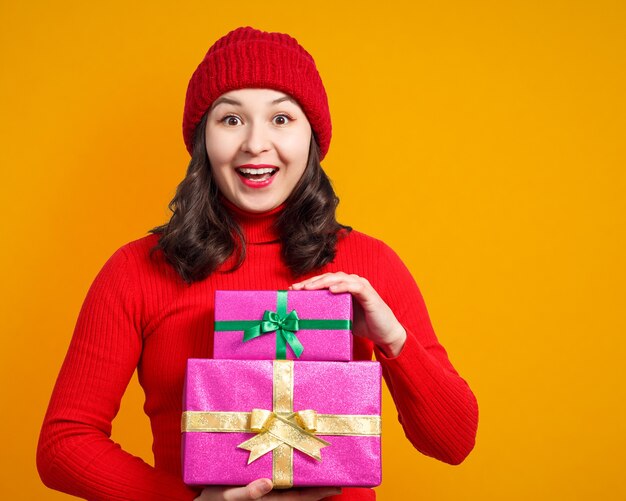 Happy woman with Christmas gifts in hands. on a yellow surface.